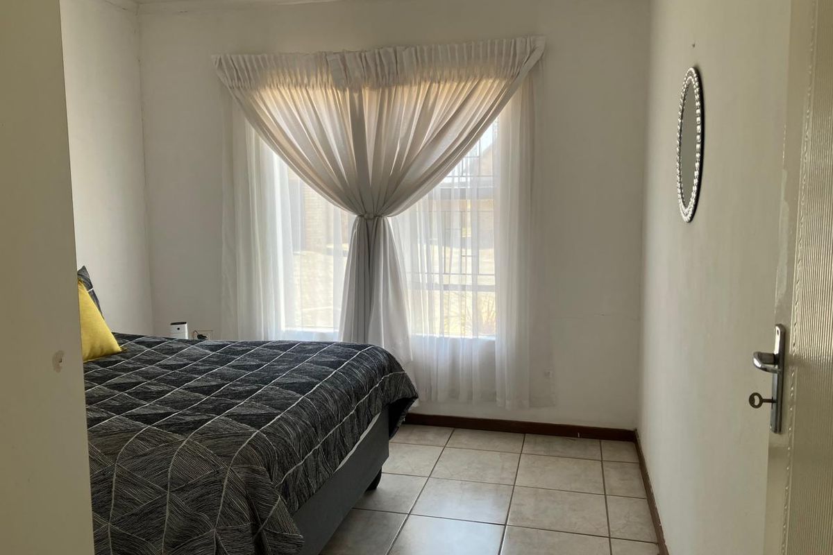 A functional bedroom featuring tiled flooring and a window with curtains, offering a neutral space ready for personalization.