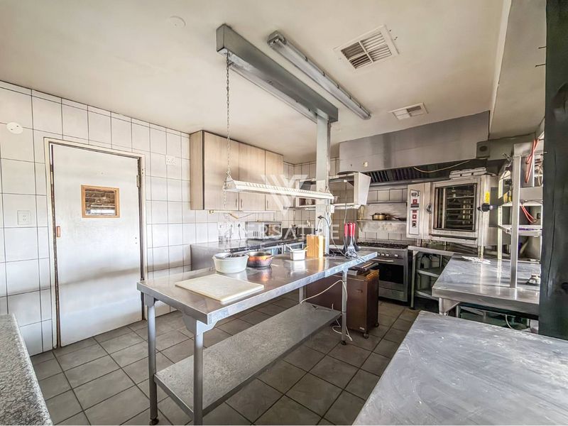 A functional commercial-style kitchen featuring stainless steel prep surfaces, built-in oven, commercial extractor hood, and tiled finishes throughout.