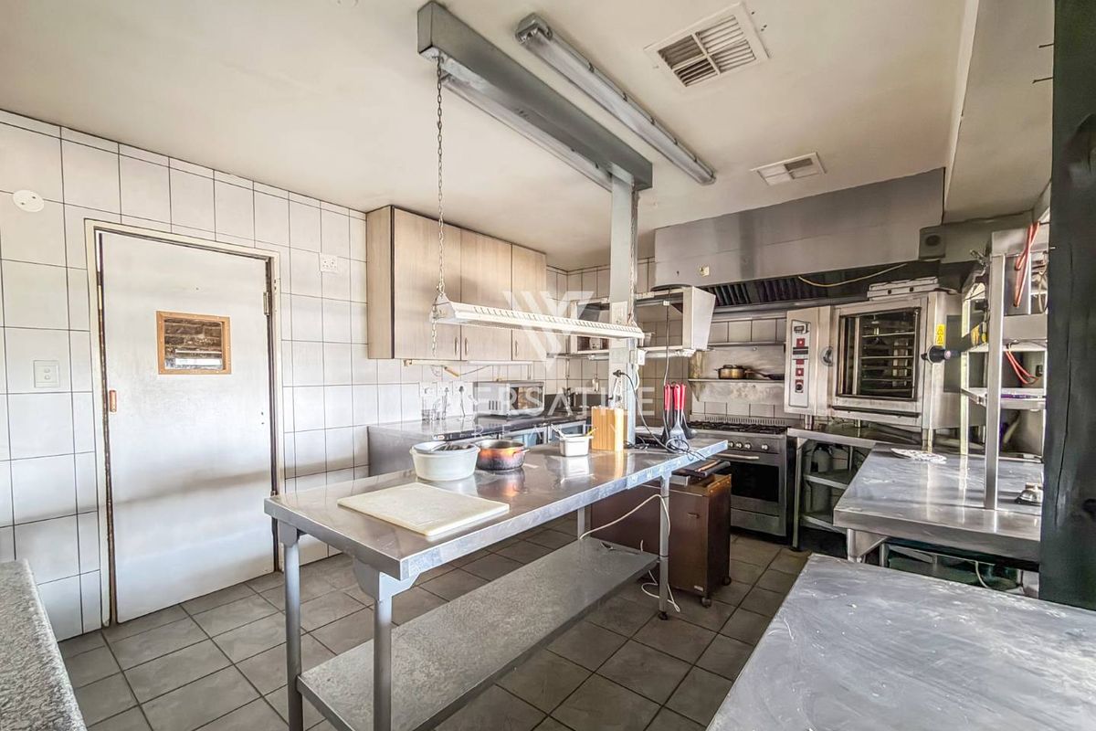 A functional commercial-style kitchen featuring stainless steel prep surfaces, built-in oven, commercial extractor hood, and tiled finishes throughout.