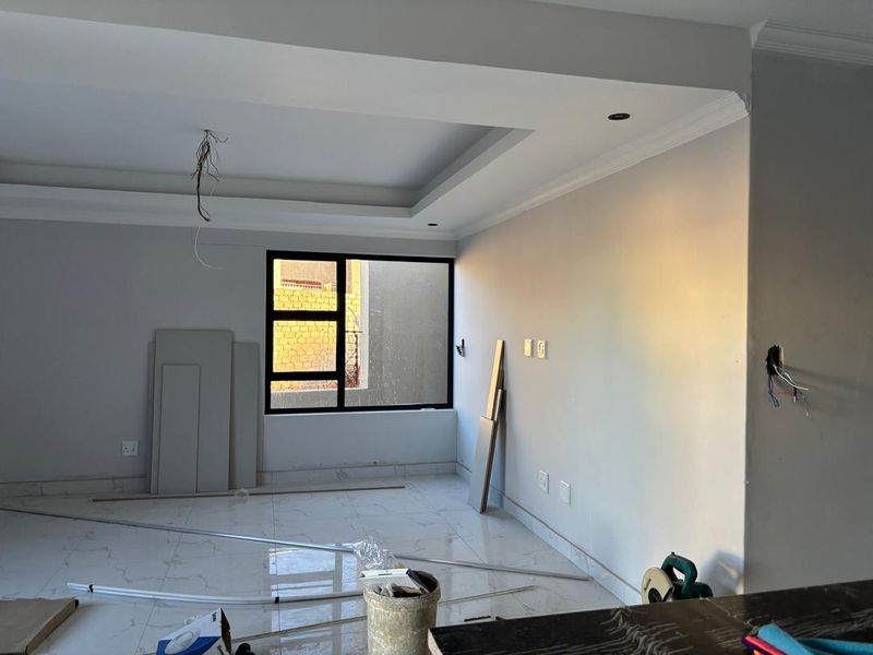 An unfinished open-plan living area featuring tiled floors, recessed ceiling details, and large aluminium-framed windows, currently undergoing renovation.