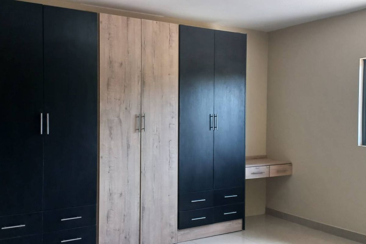 A bright bedroom featuring modern, built-in floor-to-ceiling cabinetry with a mix of dark and wood-grain finishes and integrated desk space.