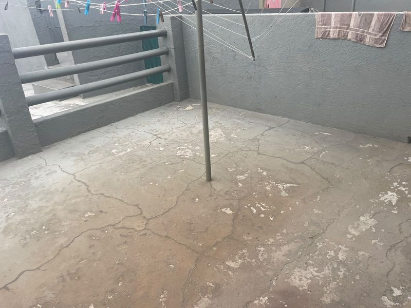 An outdoor patio area featuring a concrete floor with visible cracking and wear, enclosed by a concrete balustrade.