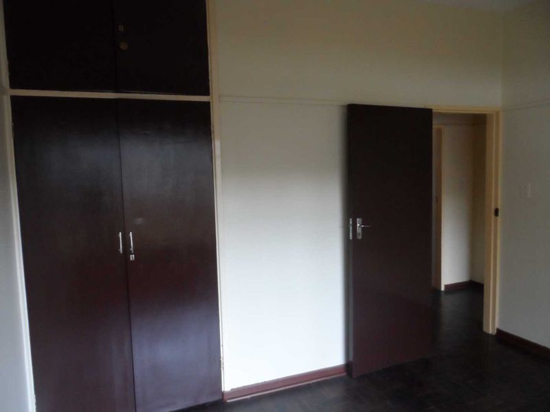 An empty bedroom featuring dark built-in cupboards and original parquet flooring, offering a blank canvas for renovation or interior design updates.