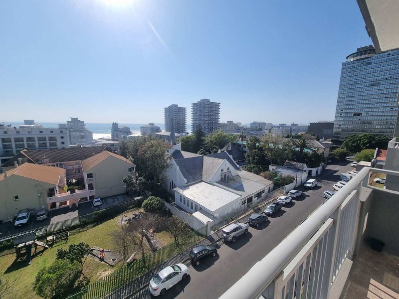 Elevated urban and coastal view overlooking the surrounding neighborhood, street, and nearby buildings from a balcony vantage point.