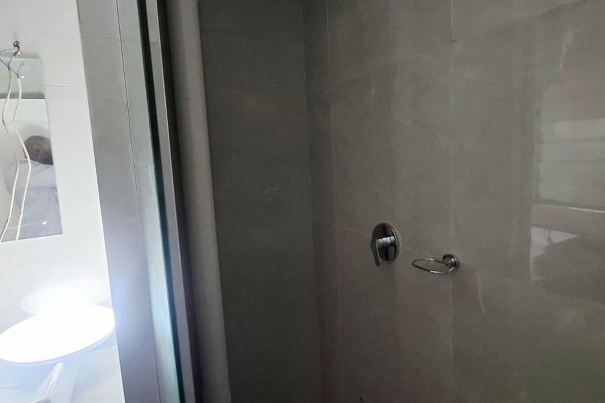A bathroom interior featuring tiled walls, a shower mixer, and a vanity area with exposed wiring and incomplete lighting installation.