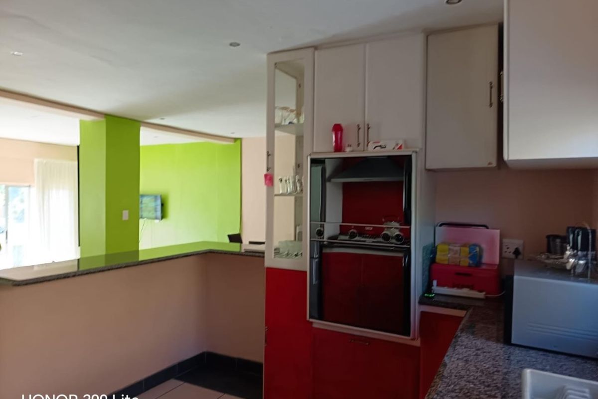 Kitchen featuring built-in oven, extractor fan, and granite countertops, opening into a living area with a breakfast bar.