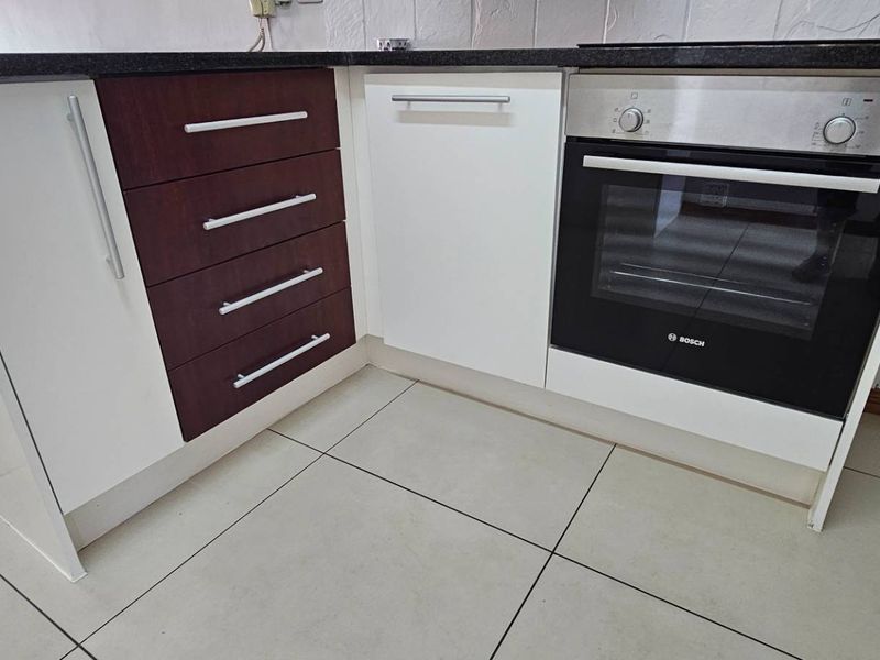 A functional kitchen area featuring built-in cabinetry, a Bosch oven, stone countertops, and tiled flooring, ready for final finishing touches.