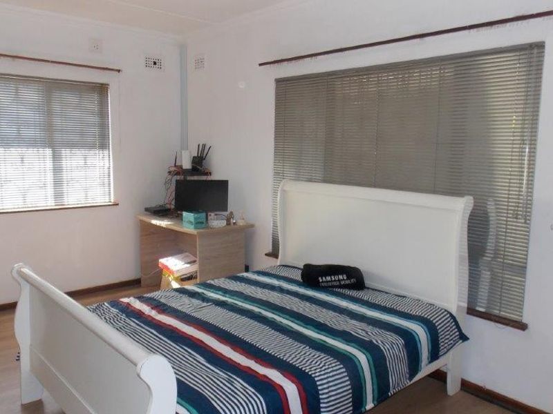 A functional bedroom featuring laminate flooring and dual windows fitted with venetian blinds, offering a neutral space ready for personalization.