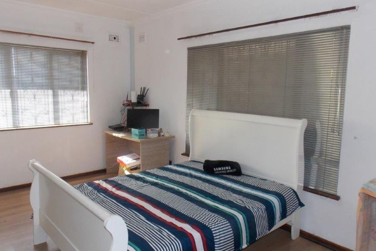 A functional bedroom featuring laminate flooring and dual windows fitted with venetian blinds, offering a neutral space ready for personalization.
