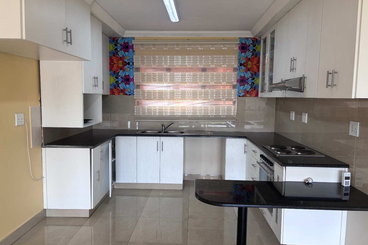 A functional kitchen featuring white cabinetry, dark granite countertops, a built-in hob, oven, extractor fan, and tiled flooring.