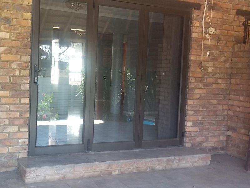 A covered patio area featuring exposed brick walls, tiled flooring, and aluminium sliding doors leading into the home.