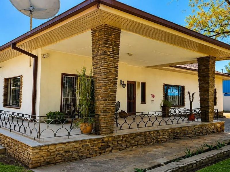 A front exterior view of a house featuring a covered patio with stone-clad pillars, metal security railings, and a paved walkway.