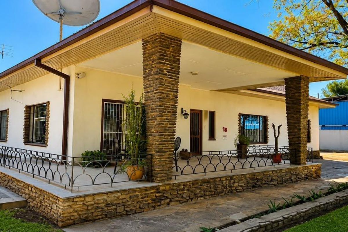 A front exterior view of a house featuring a covered patio with stone-clad pillars, metal security railings, and a paved walkway.