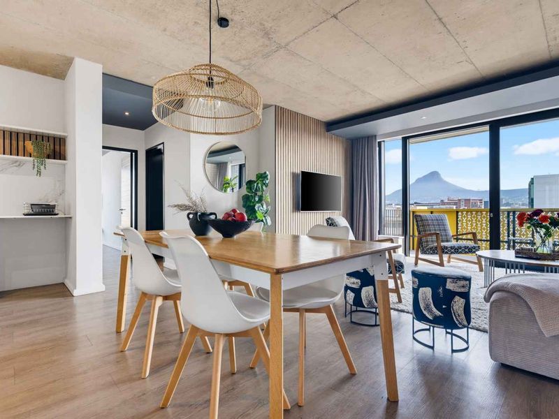 Modern open-plan living and dining area featuring an exposed concrete ceiling, timber slat wall, and seamless access to a balcony with mountain views.