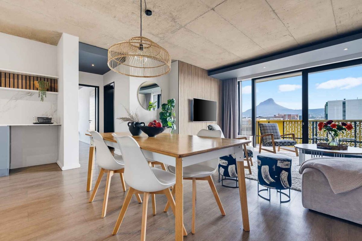 Modern open-plan living and dining area featuring an exposed concrete ceiling, timber slat wall, and seamless access to a balcony with mountain views.