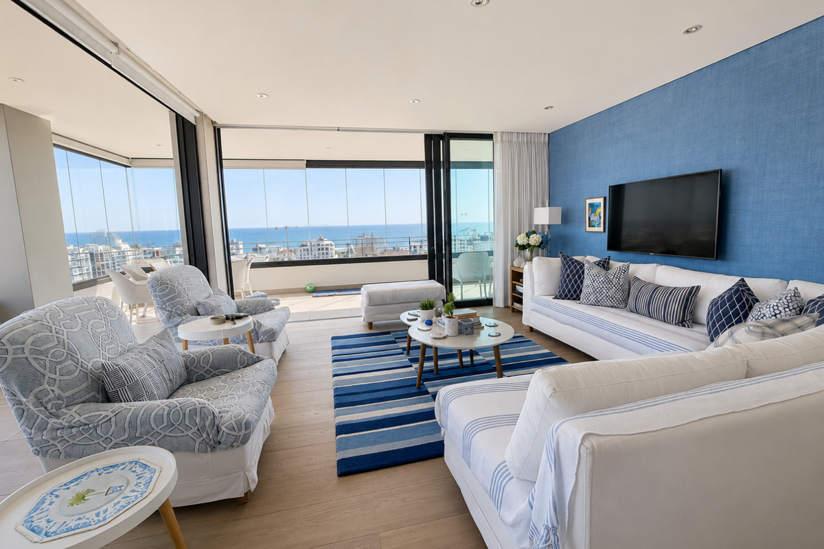 Spacious open-plan living area featuring a textured blue feature wall, recessed lighting, and seamless access to a glass-enclosed balcony with ocean views.