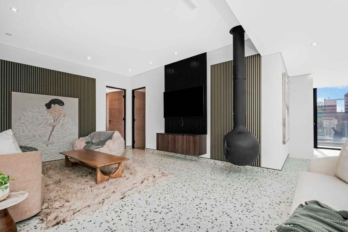 Modern living room featuring a striking suspended fireplace, terrazzo flooring, and decorative timber slat wall paneling with integrated media cabinetry.