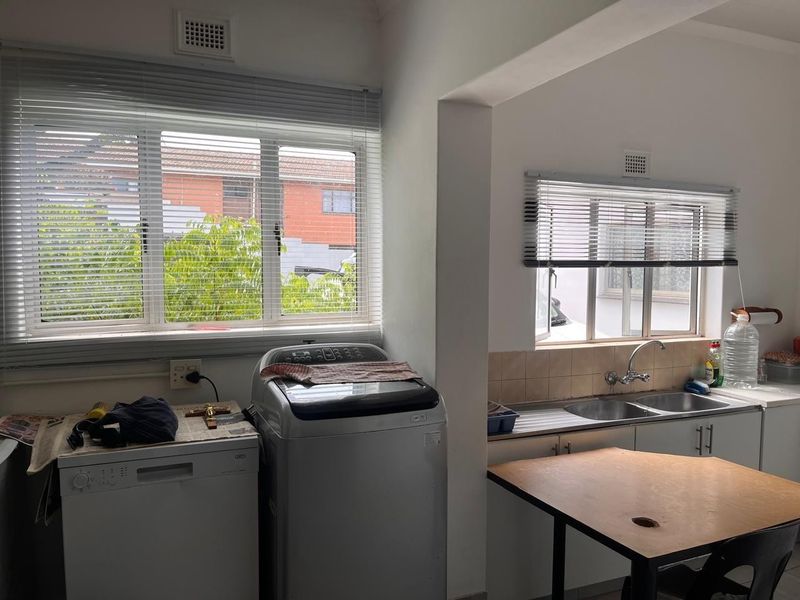 A functional scullery area featuring a double bowl sink, tiled splashback, built-in cabinetry, and dedicated space for laundry appliances.