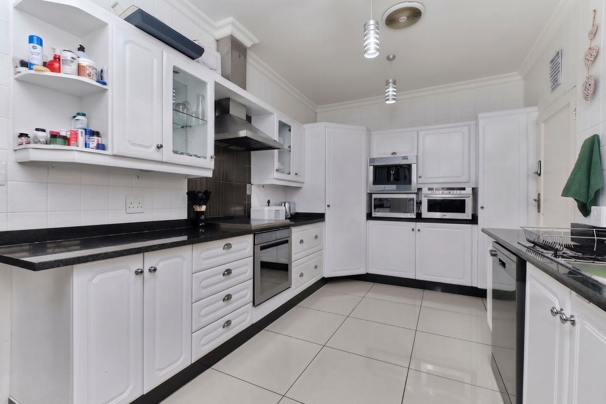 A well-maintained kitchen featuring white cabinetry, granite countertops, built-in appliances, and tiled flooring, offering a clean and functional workspace.