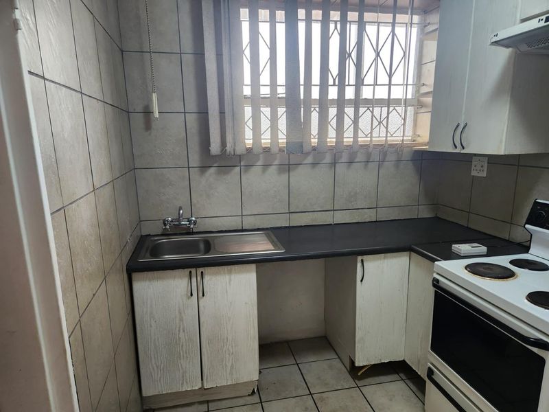 A compact kitchen featuring tiled walls and flooring, built-in cabinetry, a stainless steel sink, and a functional stove area with an extractor fan.