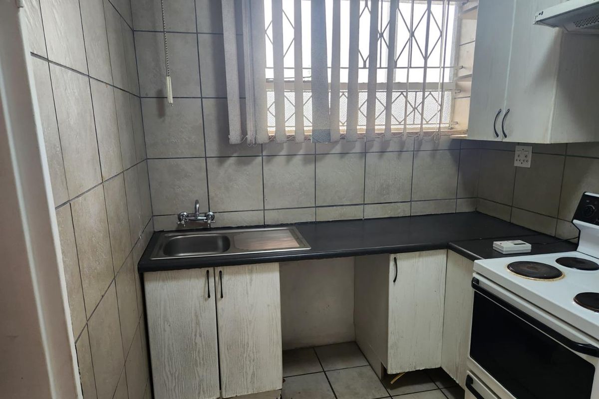 A compact kitchen featuring tiled walls and flooring, built-in cabinetry, a stainless steel sink, and a functional stove area with an extractor fan.