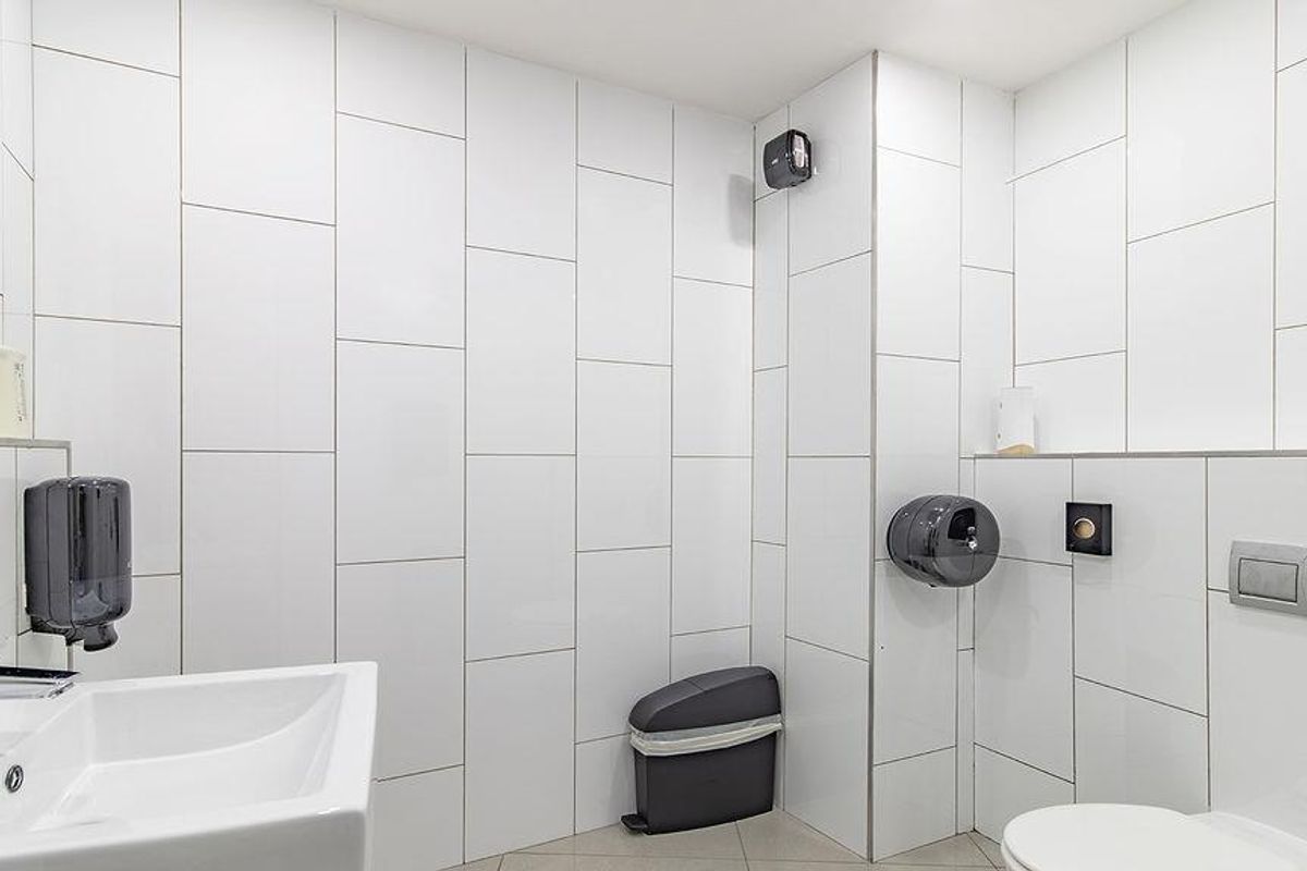 A modern, clean office restroom featuring white wall tiles, a wall-mounted basin, and a concealed cistern toilet.