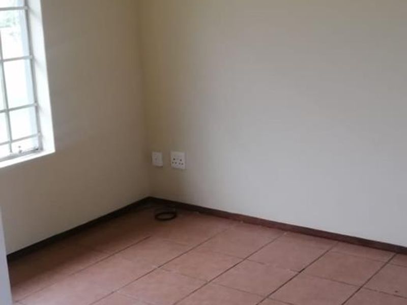 An empty bedroom featuring tiled flooring, a window with security bars, and a ceiling light fixture.
