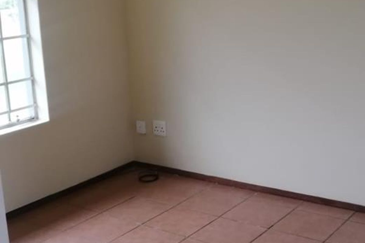 An empty bedroom featuring tiled flooring, a window with security bars, and a ceiling light fixture.