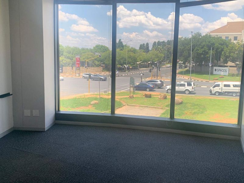 A bright, empty office space featuring large floor-to-ceiling windows with a view of the street intersection and surrounding area.