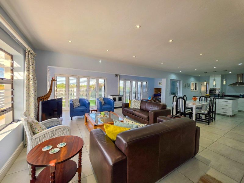 Spacious open-plan living and dining area featuring tiled floors, recessed lighting, a modern kitchen with granite countertops, and large sliding doors with plantation shutters.