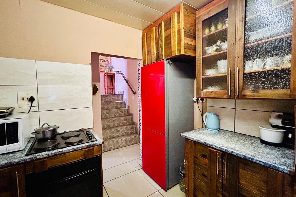 Compact kitchen featuring rustic wooden cabinetry, granite-look countertops, a built-in electric hob, and tiled flooring, with direct access to an internal staircase.