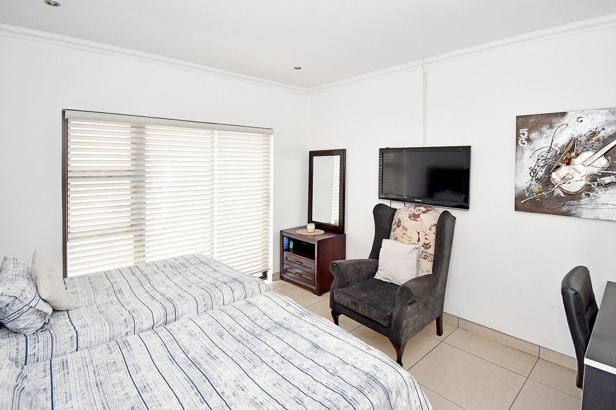 A well-maintained bedroom featuring neutral tiled flooring, coving, and large windows fitted with venetian blinds, providing a bright and functional living space.