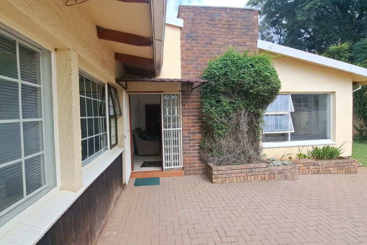 Rear exterior view of the house featuring brick paving, a brick chimney, and a secure entrance with a security gate.