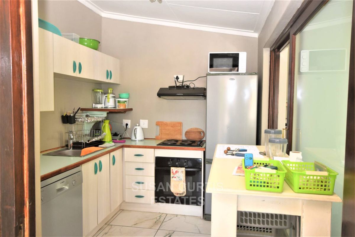 Compact kitchen featuring built-in cabinetry, integrated oven, hob, extractor fan, and tiled flooring, providing a functional workspace for a guest house.