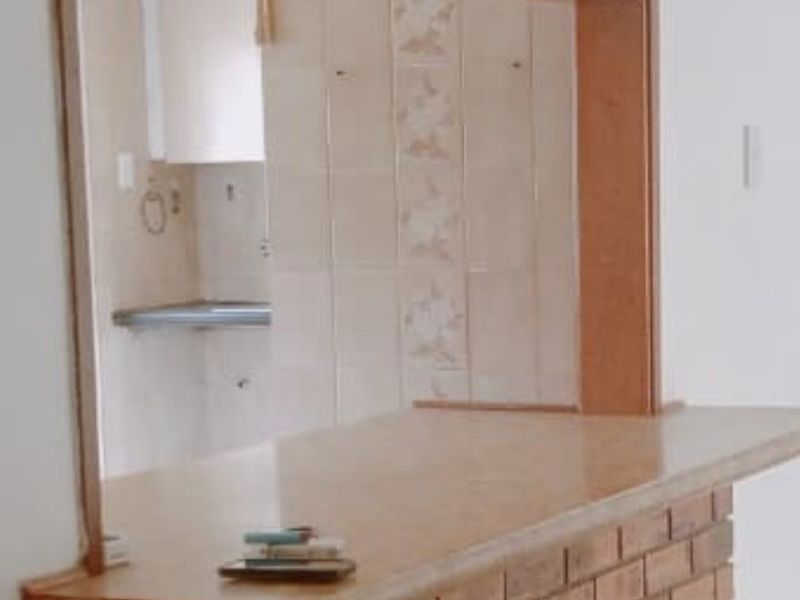 An open plan living area featuring a brick breakfast bar with a timber countertop, looking through to a tiled kitchen space.