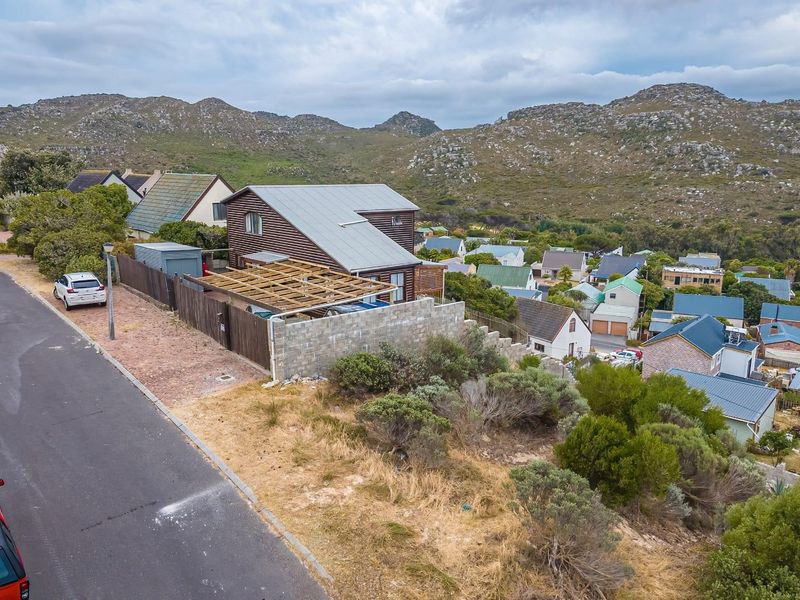 Aerial view of a residential property featuring timber cladding, a metal roof, and an unfinished timber pergola structure set against a mountain backdrop.