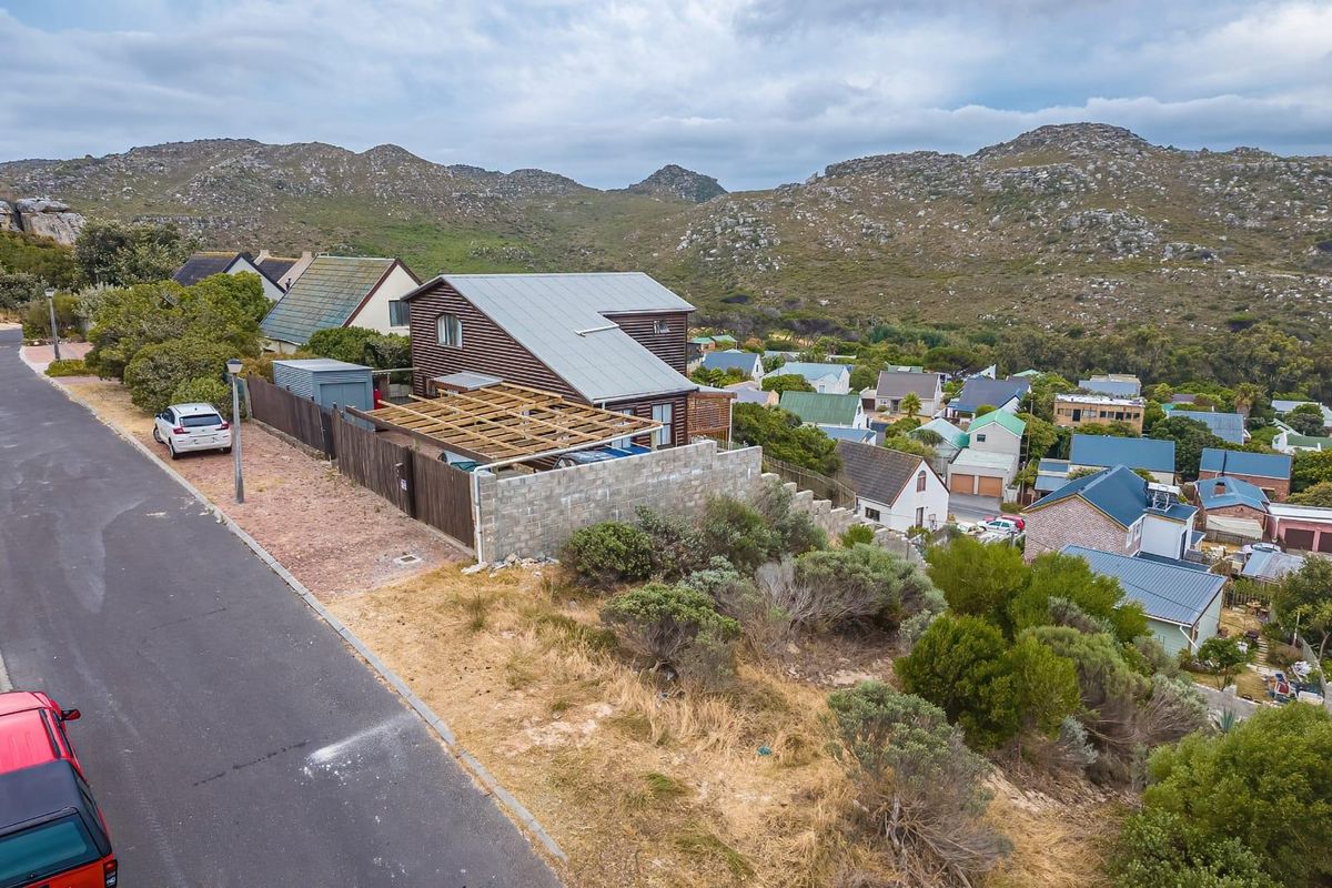 Aerial view of a residential property featuring timber cladding, a metal roof, and an unfinished timber pergola structure set against a mountain backdrop.