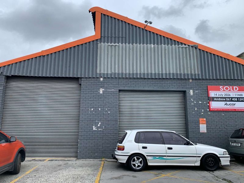 Front elevation of a commercial retail property featuring dual roller shutter doors and a corrugated metal roof structure.
