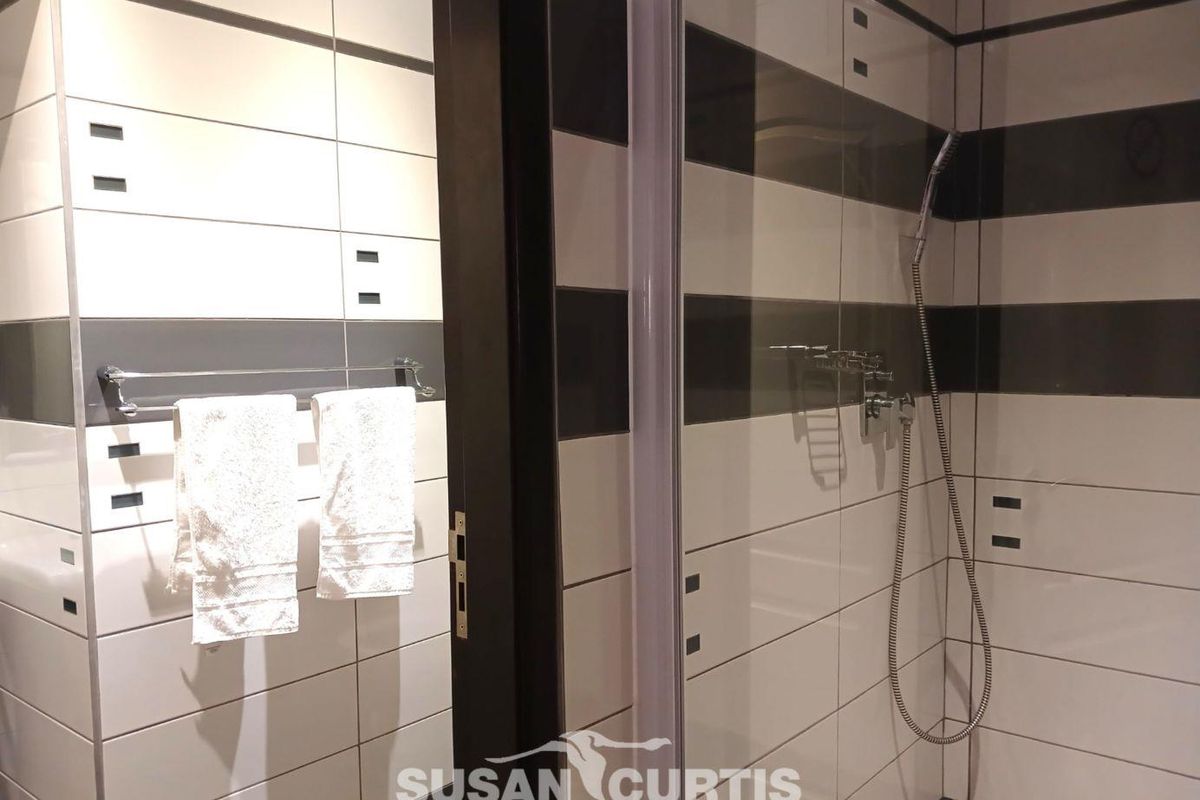 A modern bathroom featuring a glass-enclosed shower with contemporary black and white horizontal wall tiling and a chrome towel rail.
