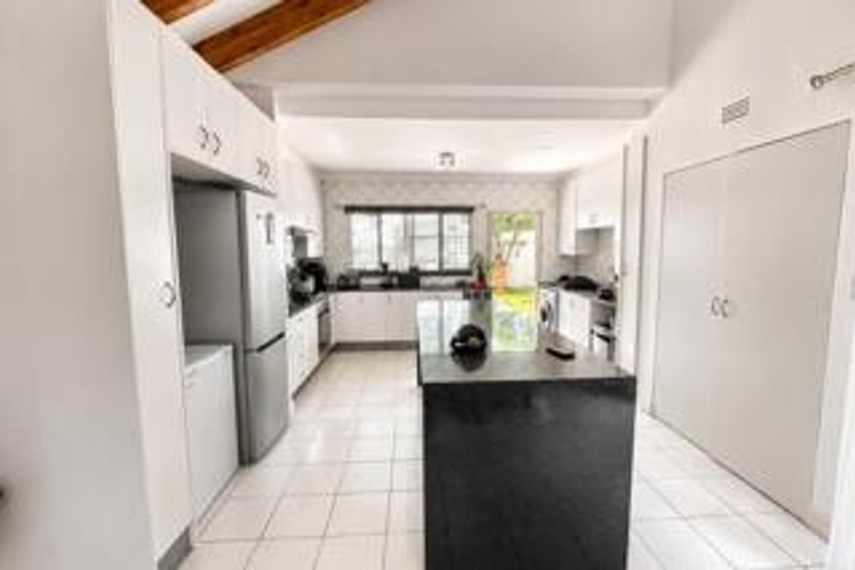 Spacious kitchen featuring a central island with granite countertop, ample built-in cabinetry, tiled flooring, and a vaulted ceiling with exposed timber beams.