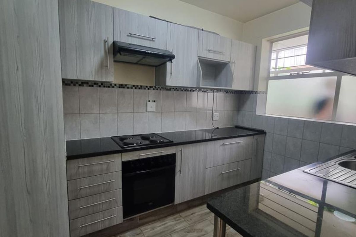 A functional kitchen featuring light wood-grain cabinetry, dark granite countertops, a built-in oven with hob, extractor fan, and tiled flooring.