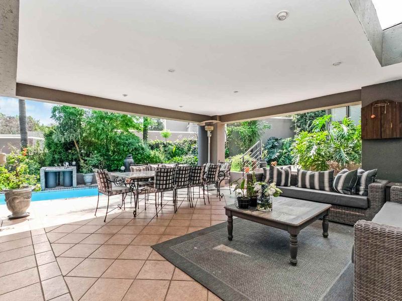 Spacious covered patio featuring tiled flooring, recessed lighting, and a built-in braai, overlooking a private swimming pool and landscaped garden area.