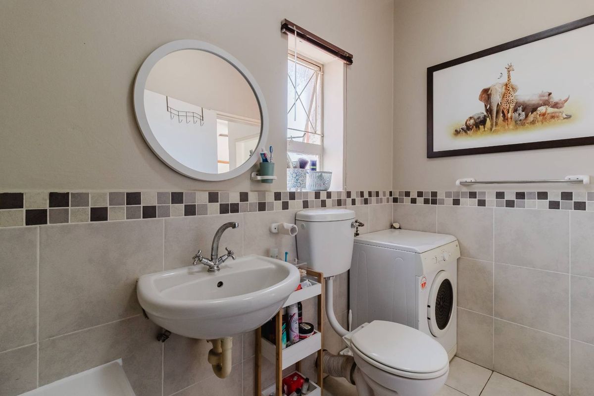 A functional bathroom featuring a wall-mounted basin, toilet, and integrated laundry space with tiled walls and a decorative mosaic border.