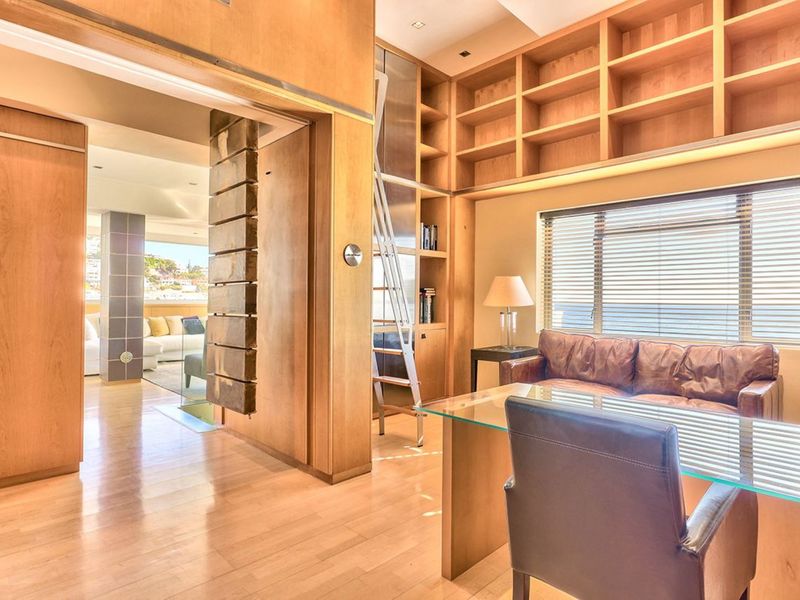A sophisticated home office featuring extensive built-in timber shelving, a sliding library ladder, and warm timber wall paneling with polished timber flooring.