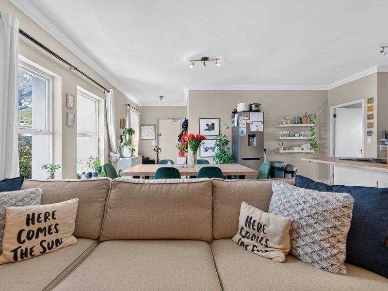 An open-plan living and dining area featuring neutral wall tones, cove cornicing, and a functional kitchen layout with integrated cabinetry and floating shelving.