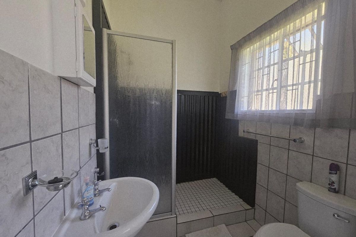 A functional bathroom featuring a walk-in shower with a glass door, pedestal basin, and toilet, finished with neutral wall and floor tiling.