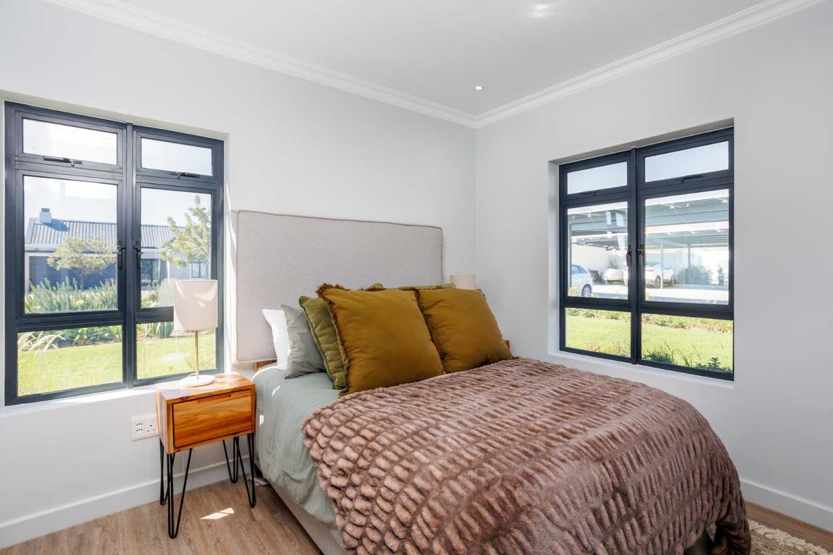 A bright and modern bedroom featuring large dark-framed windows, neutral walls, and light wood-look flooring, offering a clean and contemporary living space.