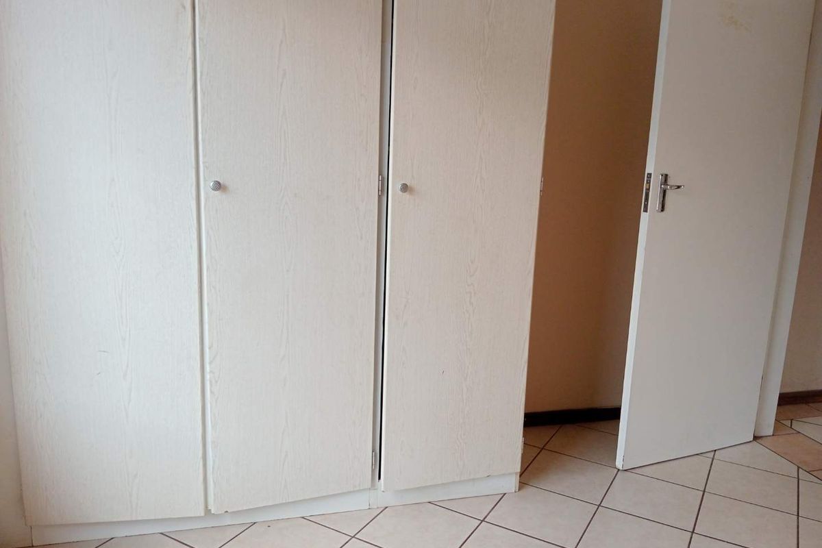A bedroom featuring built-in cupboards and tiled flooring, presented as an empty space ready for personalization.