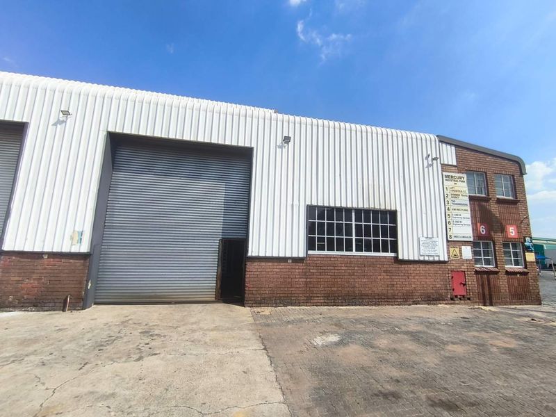 Front elevation of an industrial warehouse unit featuring a large roller shutter door, brick and metal cladding, and paved exterior access area.