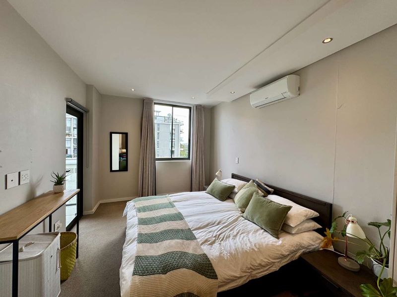 A well-maintained bedroom featuring neutral walls, carpet flooring, recessed lighting, a split-system air conditioner, and access to an outdoor balcony area.